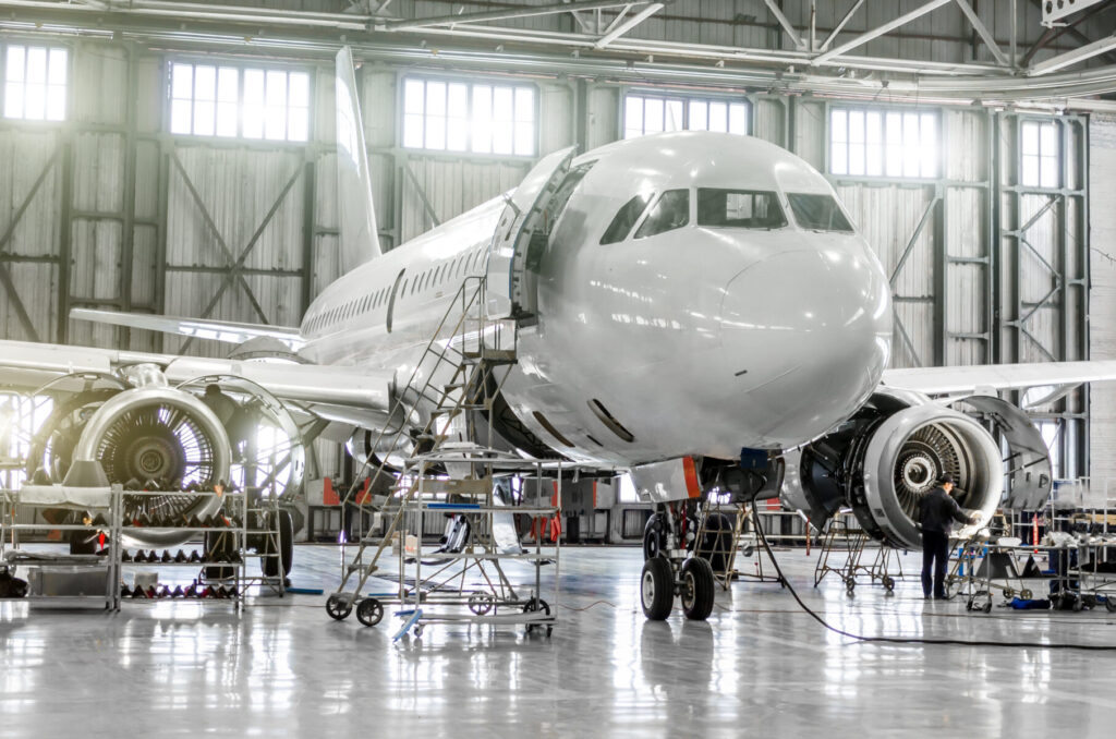 Commercial airplane undergoing maintenance in a well-lit hangar with engines exposed and workers inspecting components.