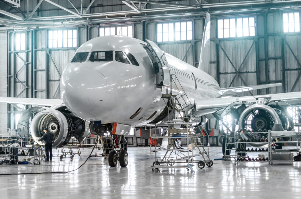 Airplane inside a hangar undergoing maintenance, with workers attending to the engines and various equipment around it.