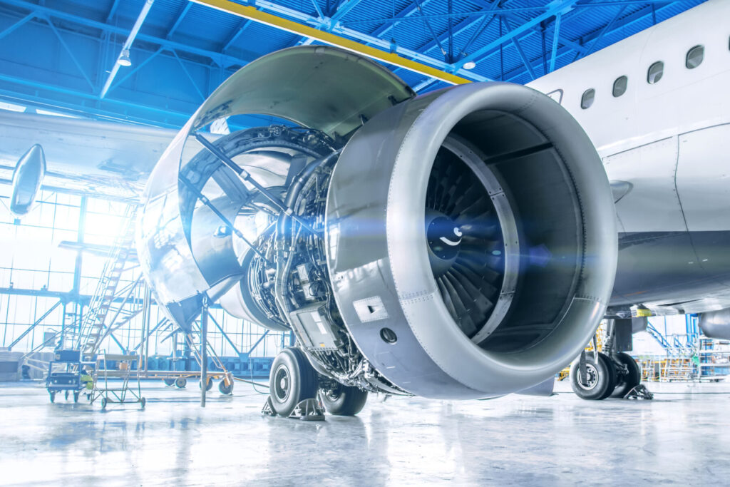 Close-up view of a jet engine in an airport hangar, with the engine cover open and maintenance equipment visible.