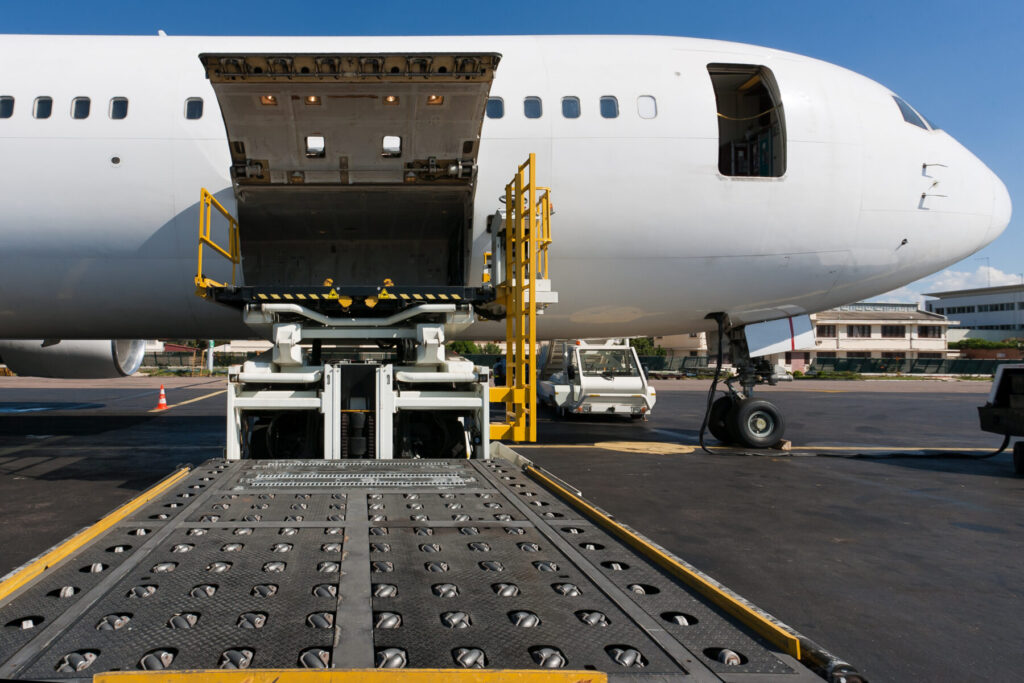 Cargo plane on tarmac with open loading bay and conveyor belt extended, ready for loading or unloading operations.